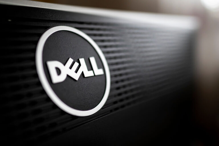 Close-up do logotipo da Dell em um equipamento eletrônico, com o emblema branco em alto relevo sobre um fundo preto texturizado. A imagem destaca a marca com iluminação suave e foco seletivo