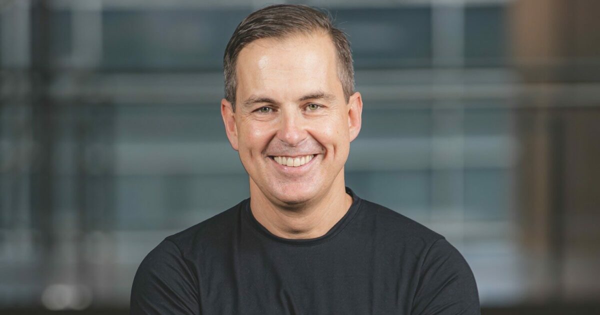 Eduardo Smith, CEO da Softplan, sorrindo em uma foto profissional. Ele veste uma camisa preta e está em um ambiente corporativo com fundo desfocado, transmitindo confiança e liderança