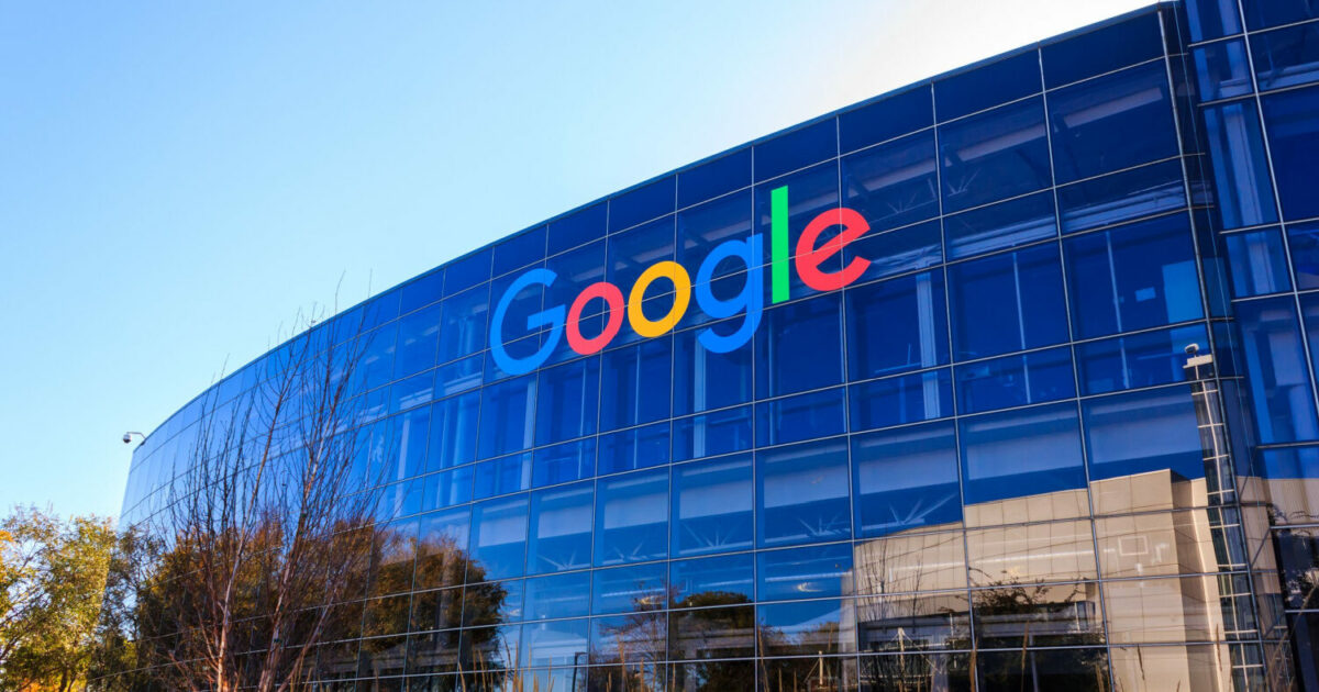 Prédio corporativo do Google com fachada de vidro refletindo o céu e árvores ao redor. O logotipo colorido do Google está em destaque na parte superior do edifício (agentspace, IA generativa, carbono)