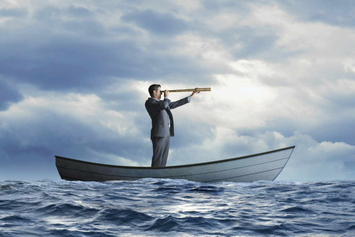 A stranded businessman standing in a rowboat in the ocean looks through a spyglass and searches the horizon for help.
