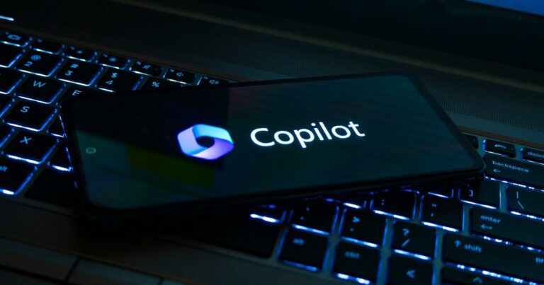 Imagem de um smartphone exibindo o logotipo e o nome 'Copilot', da Microsoft, posicionado sobre um teclado retroiluminado, representando inovação e integração tecnológica. (microsoft)