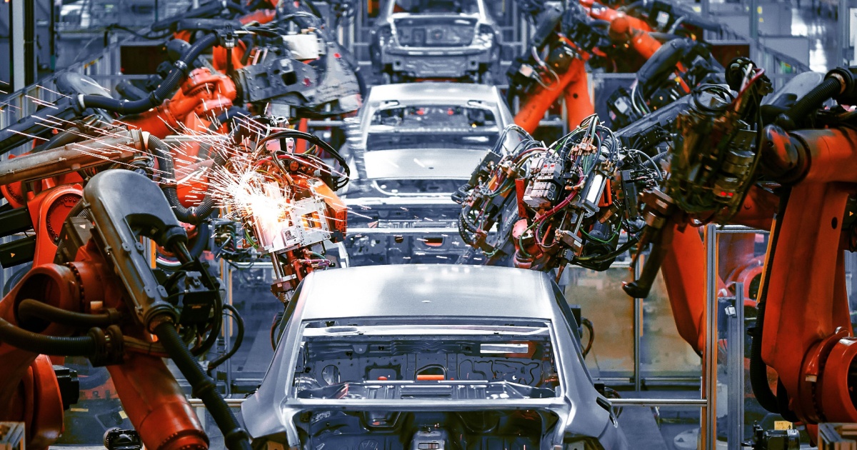 A imagem mostra uma linha de montagem de automóveis, onde diversos veículos em estágios diferentes de montagem estão alinhados. Robôs industriais estão envolvidos no processo, evidenciando a automação na fabricação de automóveis. O ambiente é industrial e bem iluminado, com uma predominância de cores metálicas e tons frios. Essa cena representa a modernização e eficiência do setor automotivo, destacando o uso de tecnologia avançada na produção.