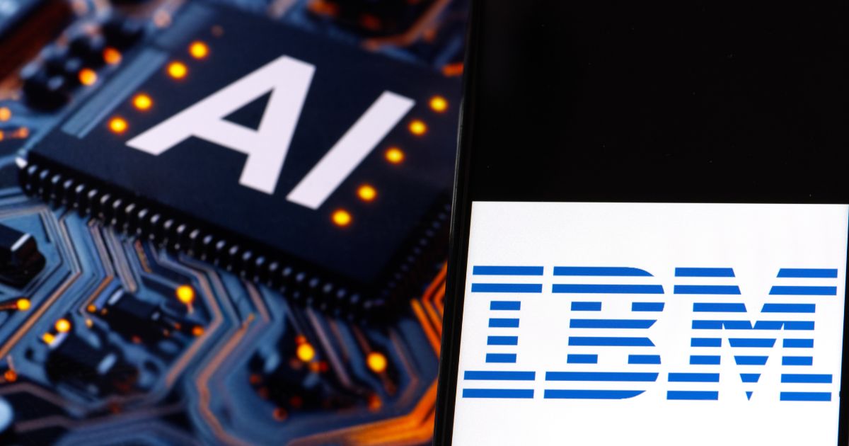 A imagem mostra dois elementos principais lado a lado. À esquerda, há uma representação de um chip eletrônico com a palavra "AI" (sigla para inteligência artificial) impressa em branco, sobre um fundo preto. O chip está inserido em uma placa de circuito com vários pontos de luz laranja ao redor, destacando seu funcionamento tecnológico. À direita, aparece o logotipo da IBM, com o texto "IBM" em azul em estilo icônico, sobre um fundo branco. A combinação dos dois elementos simboliza a associação da IBM com tecnologias de inteligência artificial.