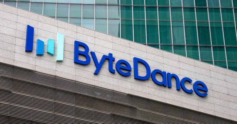 A imagem mostra a fachada de um prédio com o logotipo da ByteDance, empresa de tecnologia conhecida por ser a criadora do TikTok. O logotipo é composto pela palavra "ByteDance" em letras azuis, com um gráfico de barras coloridas (verde e azul) ao lado esquerdo, representando um crescimento ou progresso. O fundo da imagem mostra uma parede de vidro reflexiva, dando um toque moderno e corporativo ao ambiente