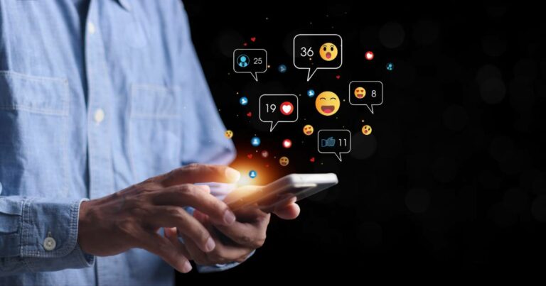 Pessoa utilizando um smartphone enquanto ícones de interações digitais, como curtidas, comentários e reações com emojis, flutuam ao redor da tela. O fundo escuro destaca a luminosidade dos ícones, representando o engajamento em redes sociais e o impacto da tecnologia na comunicação, abx, hiperpersonalização ( IA generativa), ABM