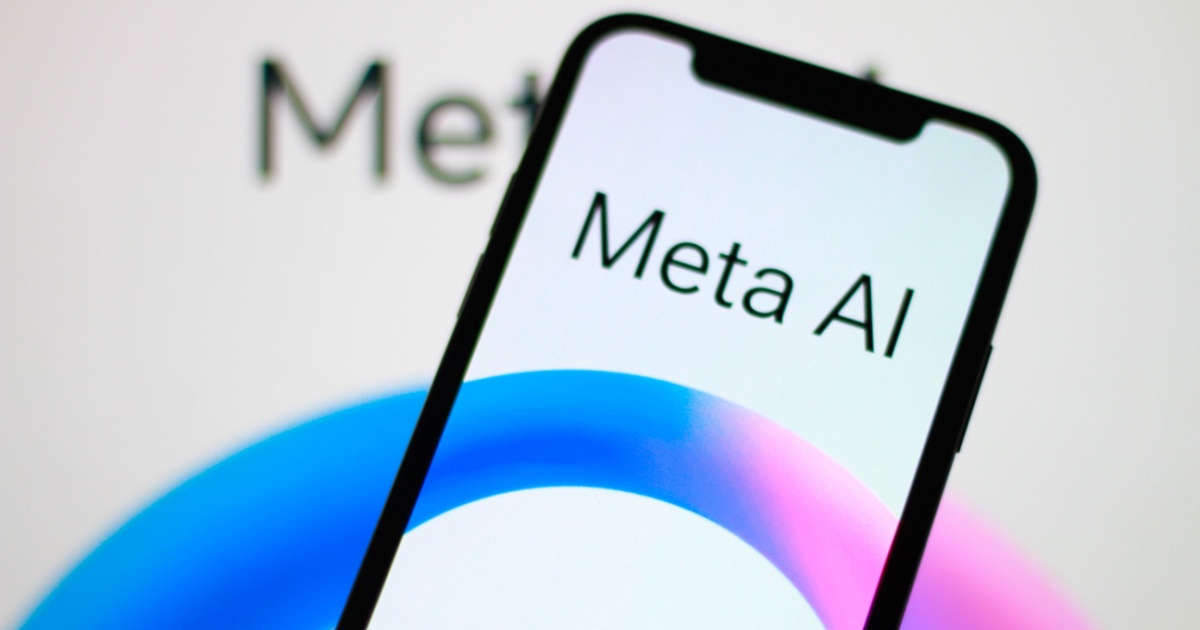 Smartphone exibindo a tela com o texto 'Meta AI' sobre um fundo colorido em tons de azul e rosa. Ao fundo, o logotipo da Meta é parcialmente visível, destacando tecnologias de inteligência artificial desenvolvidas pela empresa (meta ai, whatsapp, meta)