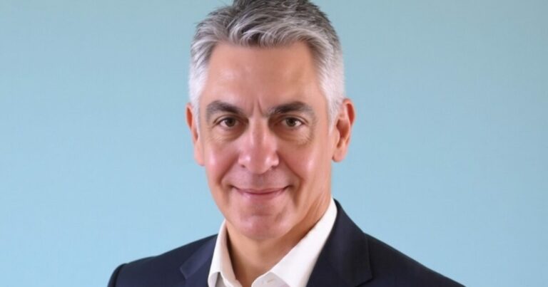 Adriano Picchi Neves, novo presidente da Avanade no Brasil, em uma foto profissional. Ele veste um terno escuro com camisa branca e aparece sorrindo, com fundo azul claro, transmitindo profissionalismo e confiança