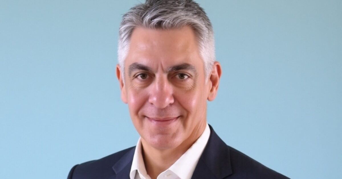 Adriano Picchi Neves, novo presidente da Avanade no Brasil, em uma foto profissional. Ele veste um terno escuro com camisa branca e aparece sorrindo, com fundo azul claro, transmitindo profissionalismo e confiança