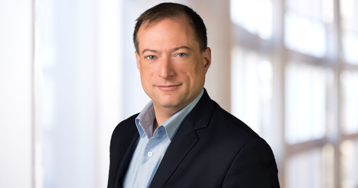 John Roese, Chief Technology Officer (CTO) e Chief AI Officer (CAIO) global da Dell Technologies, em uma foto profissional. Ele veste um terno escuro com camisa azul clara, posando com expressão confiante e fundo desfocado de ambiente corporativo