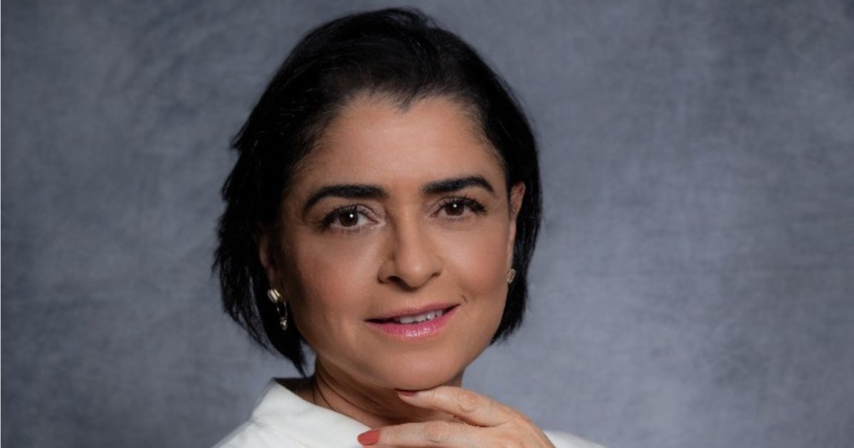 A imagem mostra Josilda Saad, executiva atuando como CIO na Suzano, em um retrato profissional de close. Ela possui cabelos curtos e escuros, arrumados de forma alinhada e rente à cabeça. Seu rosto apresenta sobrancelhas bem definidas, olhos castanhos expressivos e um leve sorriso nos lábios, realçado por uma maquiagem suave e discreta. Ela usa brincos pequenos, de metal, que complementam o visual sóbrio e elegante. A fotografia foi tirada diante de um fundo neutro em tom acinzentado, o que ajuda a destacar os traços do rosto e a expressão serena e confiante da executiva. A posição da mão, apoiando levemente o queixo, transmite uma sensação de ponderação e profissionalismo (microsoft)