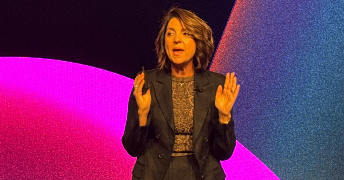 Paula Bellizia, VP Latam da AWS no reinvent 2024. Paula veste preto em um fundo roxo e rosa.