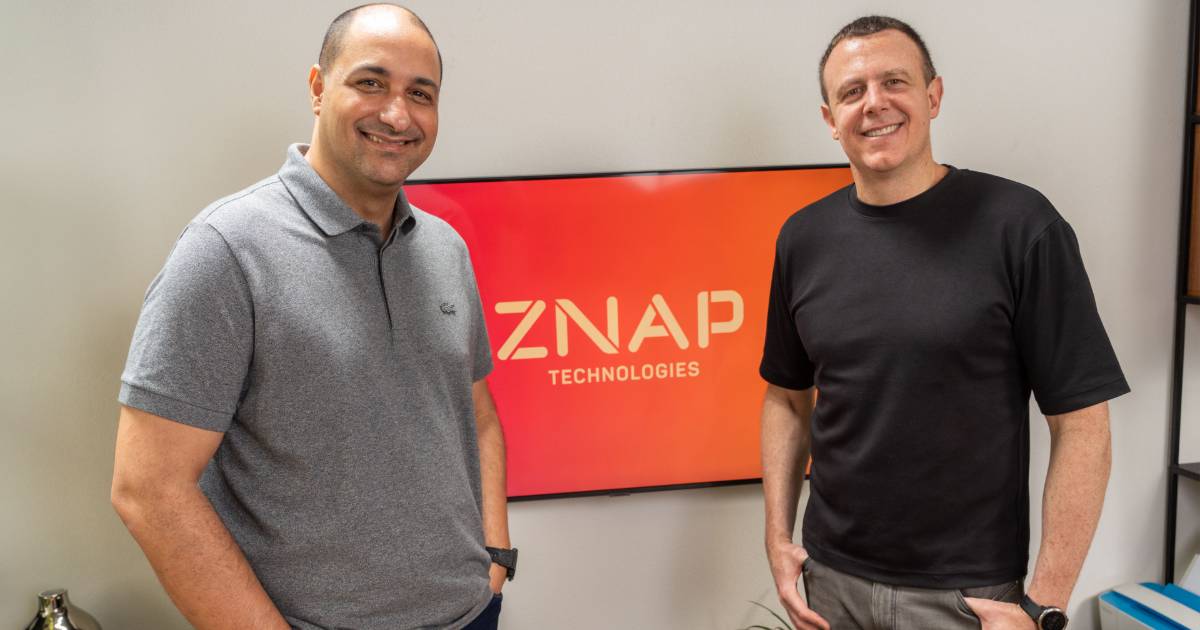 Luciano de Medeiros, CTO, e Ricardo Junqueira, CEO, da ZNAP Technologies, posam sorrindo em frente a um monitor que exibe o logotipo da empresa em fundo vermelho. Ambos estão em um ambiente moderno, transmitindo profissionalismo e inovação