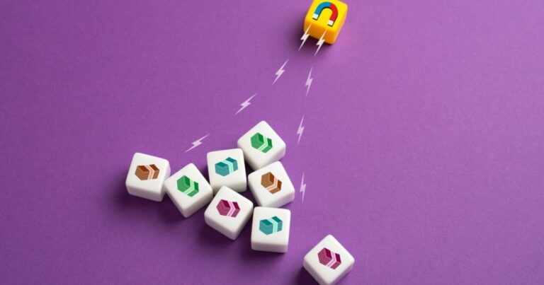 A imagem apresenta um fundo roxo vibrante e contém um conjunto de peças quadradas brancas com ícones coloridos estilizados, organizados de forma irregular. No canto superior direito, um pequeno cubo amarelo com um desenho de um ímã em vermelho e azul parece atrair essas peças, simbolizado por linhas pontilhadas ou raios que representam magnetismo. A composição transmite a ideia de atração, organização ou impacto de forças invisíveis em elementos variados.