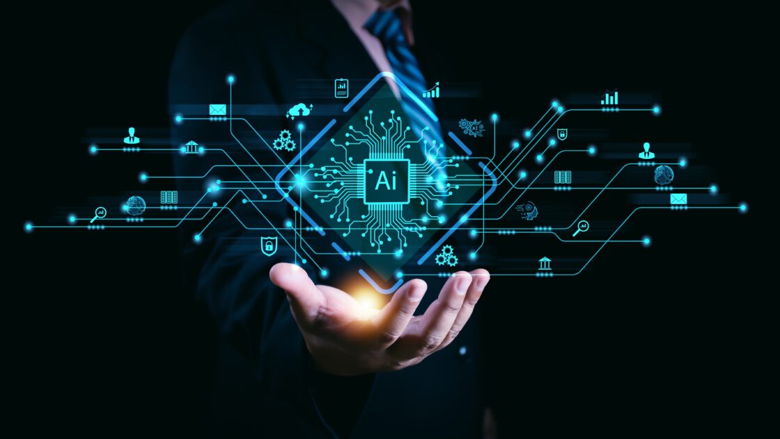 Uma mão estendida segurando uma representação holográfica de um chip de inteligência artificial (AI) no centro, rodeado por linhas e ícones tecnológicos que simbolizam conectividade, como engrenagens, gráficos, globos e cadeados. O fundo é escuro, destacando o brilho azul do holograma, humana (Brasil, shadow, Nvidia)