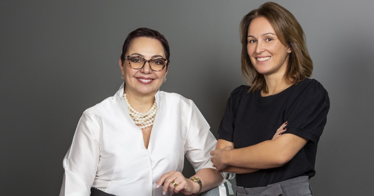 Tania Cosentino, com blusa branca e colar de pérolas, e Priscyla Laham, vestindo blusa preta, posam juntas em frente a um fundo cinza. Ambas sorriem, representando suas novas posições na Microsoft: Tania como gerente geral de Vendas para o Setor de Segurança na América Latina e Priscyla como presidente da Microsoft Brasil