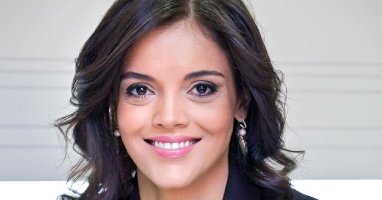 Retrato de Ana Paula Assis, nova vice-presidente sênior da IBM para a região EMEA (Europa, Oriente Médio e África). Na imagem, ela aparece sorridente, com cabelos castanhos ondulados, usando brincos de pérola e vestindo traje formal, transmitindo uma postura profissional e acolhedora. O fundo é claro e neutro, destacando o foco na executiva