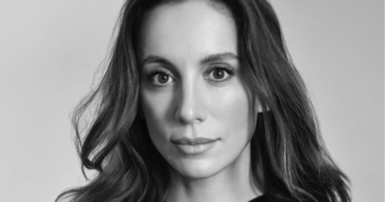 A imagem é um retrato em preto e branco de Mira Murati, ex-CTO da OpenAI. Ela aparece de frente para a câmera, com uma expressão serena e olhar direto. Seus cabelos longos e ondulados emolduram seu rosto, e sua pele tem uma textura suave, realçada pela iluminação equilibrada. O fundo é simples e neutro, destacando ainda mais seus traços faciais