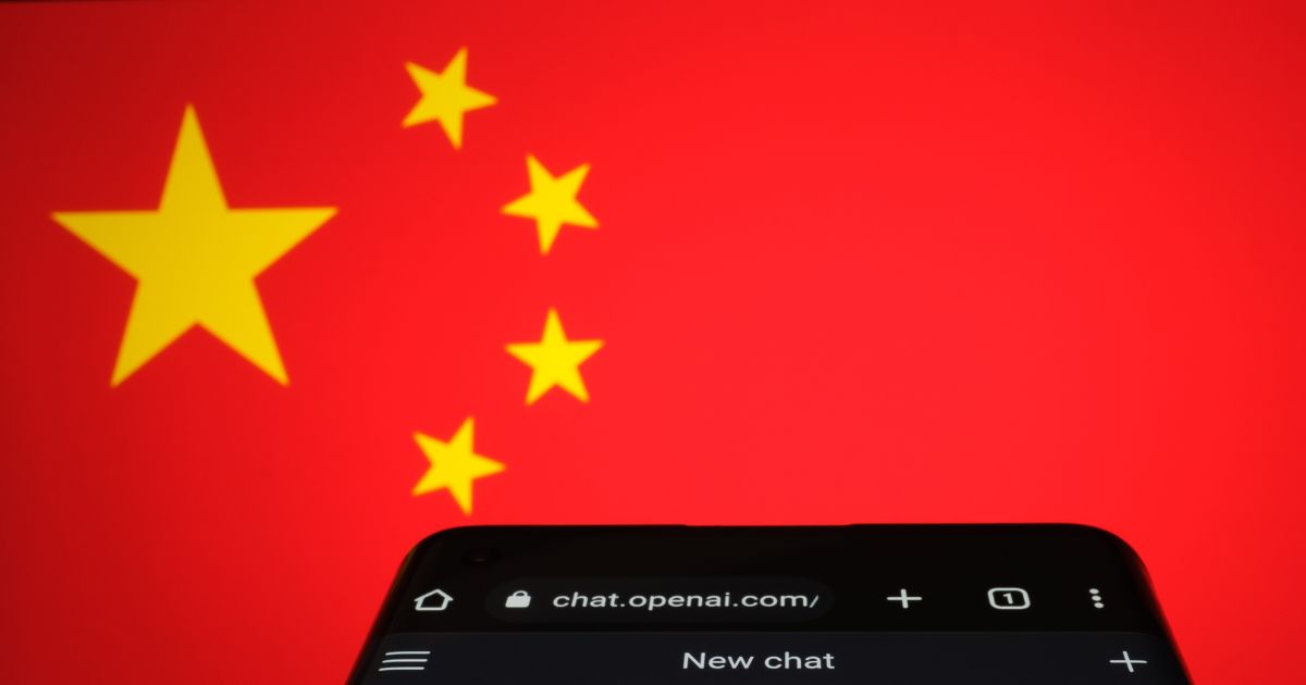 Uma fotografia mostra um smartphone com a tela aberta no site 'chat.openai.com', sugerindo o acesso ao ChatGPT. No fundo, há a bandeira da China, que possui um fundo vermelho com cinco estrelas amarelas no canto superior esquerdo. A imagem transmite uma conexão entre o uso do ChatGPT e a China.