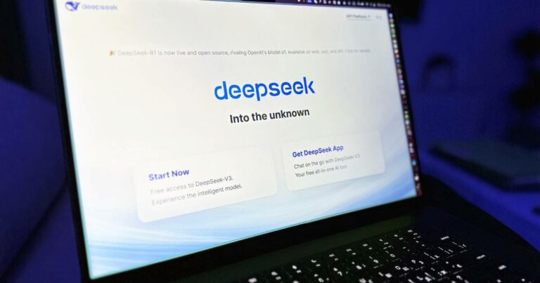 Imagem de um laptop com a tela mostrando a interface da DeepSeek. O título 'DeepSeek' aparece em destaque com o subtítulo 'Into the unknown' logo abaixo, em um fundo branco com tons suaves de azul. Há botões na interface com as opções 'Start Now' e 'Get DeepSeek App', incentivando o uso gratuito e o download do aplicativo. O ambiente ao redor está escuro, criando contraste com a tela iluminada (Europa)