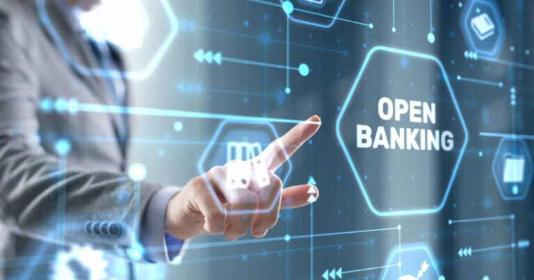 Imagem conceitual sobre Open Banking. Uma mão apontando para um painel digital com o texto 'OPEN BANKING' destacado em um hexágono luminoso. O fundo apresenta ícones tecnológicos e conexões digitais em tons de azul, representando a integração e o compartilhamento de dados financeiros de forma segura e transparente, consentimentos (fintech)