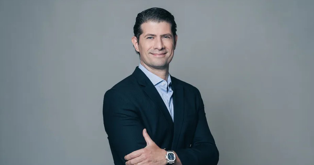 A imagem mostra Orlando Cintra, da BR Angels, posando para um retrato profissional. Ele veste um terno escuro sobre uma camisa social clara e exibe um leve sorriso. Seus braços estão cruzados, transmitindo uma postura confiante. O fundo é neutro e simples, destacando o sujeito na fotografia (agro)