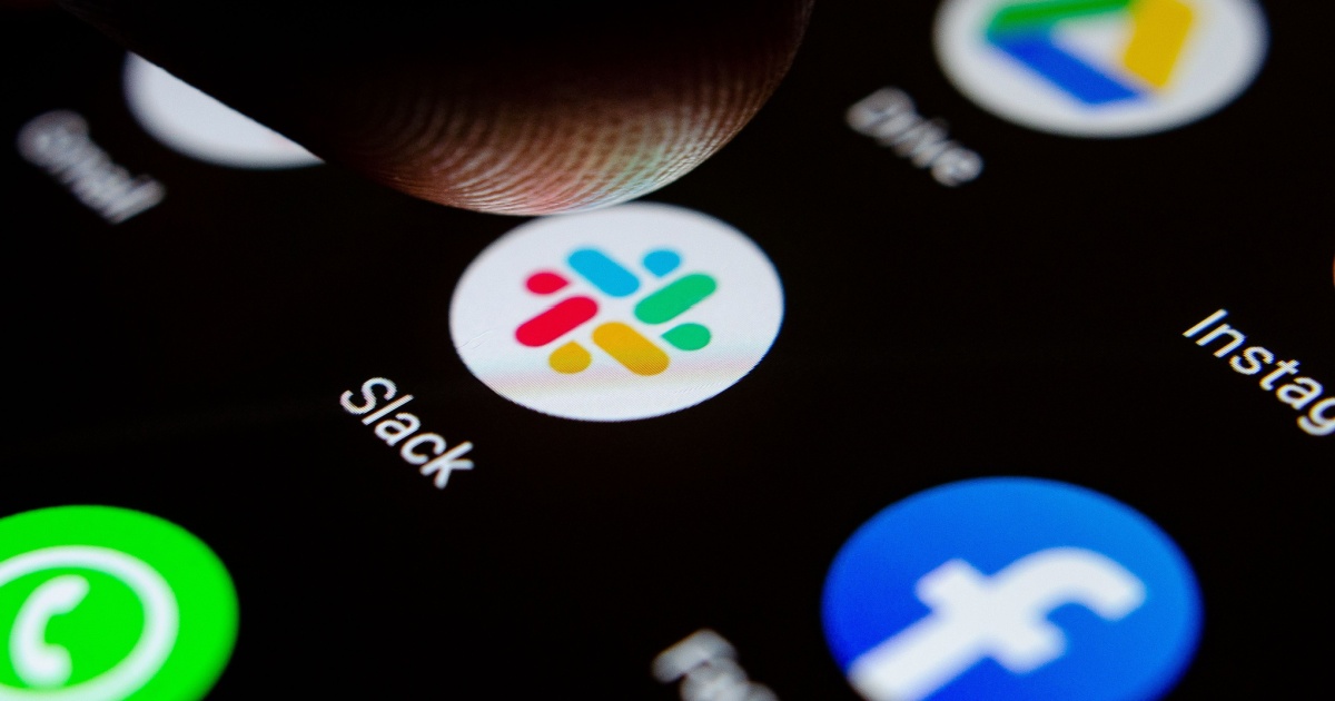 A imagem mostra uma tela de smartphone com o ícone do aplicativo Slack em destaque. Um dedo está prestes a tocar no ícone, indicando uma interação iminente. Outros aplicativos, como WhatsApp, Facebook, Instagram e Google Drive, também são visíveis ao redor, sugerindo um ambiente digital de comunicação e produtividade. A foto tem um foco fechado, destacando a textura do dedo e a nitidez dos ícones (slack, app, Jeitto)