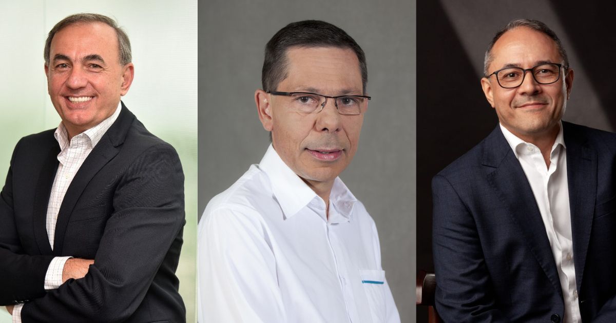Montagem com três retratos de homens de meia-idade, cada um em um fundo diferente. O homem à esquerda veste um blazer preto sobre uma camisa branca e sorri de braços cruzados contra um fundo esverdeado claro. O homem ao centro usa óculos e uma camisa branca com um pequeno detalhe azul no bolso, olhando seriamente para a câmera contra um fundo cinza. O homem à direita veste um blazer azul escuro sobre uma camisa branca, usa óculos e sorri levemente, posando contra um fundo escuro com iluminação dramática.