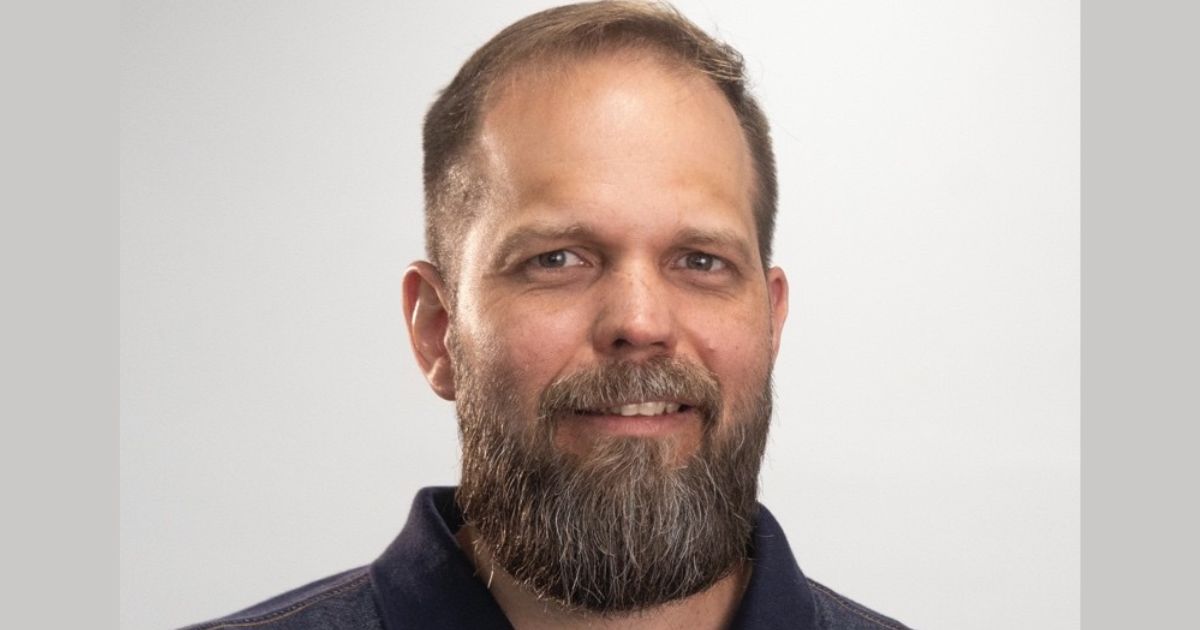 Homem adulto com barba cheia e cabelo curto, a sorrir ligeiramente para a câmara, com fundo neutro e iluminação suave.