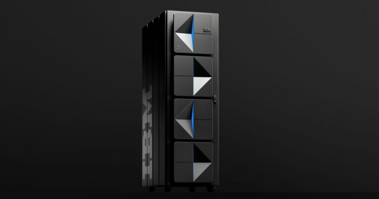 Computador de grande porte da IBM, modelo IBM Z, com design moderno e painéis frontais geométricos em preto, branco e azul. O equipamento está posicionado num fundo preto minimalista, destacando o seu aspeto tecnológico e sofisticado. Na lateral, é possível ver a marca “IBM” em letras grandes e prateadas.