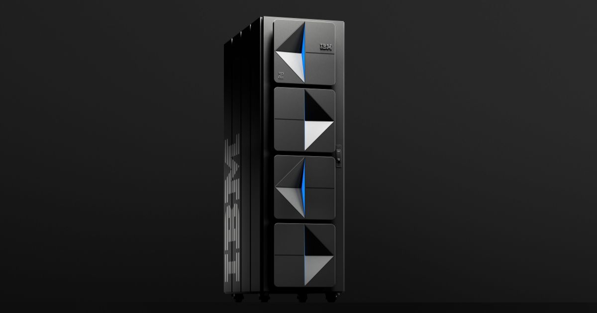 Computador de grande porte da IBM, modelo IBM Z, com design moderno e painéis frontais geométricos em preto, branco e azul. O equipamento está posicionado num fundo preto minimalista, destacando o seu aspeto tecnológico e sofisticado. Na lateral, é possível ver a marca “IBM” em letras grandes e prateadas.