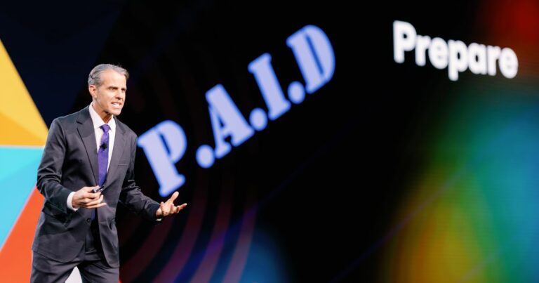 Imagem de Eric O'Neil, especialista em cibersegurança e ex-operador do FBI, durante sua palestra no evento VeeamON 2025. Ele está de terno escuro e gravata roxa, gesticulando enquanto fala no palco. Ao fundo, vê-se uma tela com a palavra "P.A.I.D" em destaque e o termo "Prepare" parcialmente visível, indicando o conteúdo de sua apresentação (hacker)