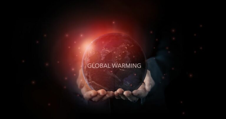 Imagem simbólica de duas mãos a segurar um globo terrestre iluminado por uma luz vermelha intensa, representando o aquecimento global. No centro do planeta, em destaque, aparece o texto 'GLOBAL WARMING'. O fundo é escuro, com pequenas partículas luminosas espalhadas, sugerindo calor ou partículas no espaço.