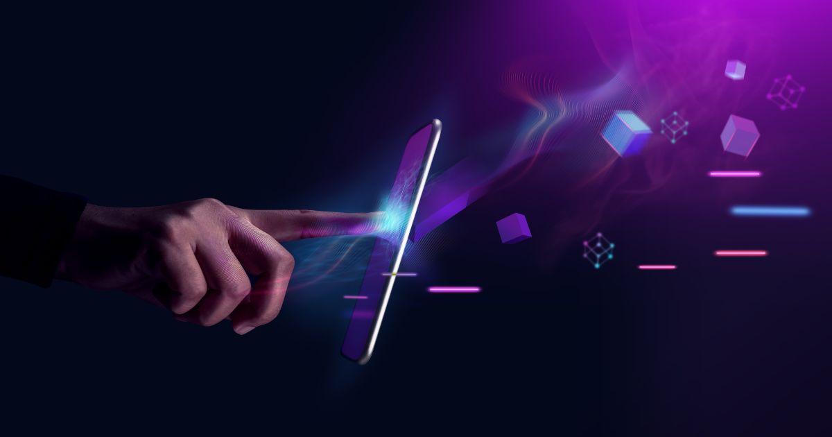 Imagem digital abstrata de uma mão a tocar num ecrã de smartphone flutuante, com efeitos de luz a simular interações tecnológicas. Do outro lado do ecrã, elementos gráficos tridimensionais, como cubos e linhas luminosas em tons de roxo, azul e rosa, emergem para simbolizar dados, inovação e realidade digital aumentada. O fundo é escuro, criando contraste com os efeitos vibrantes.