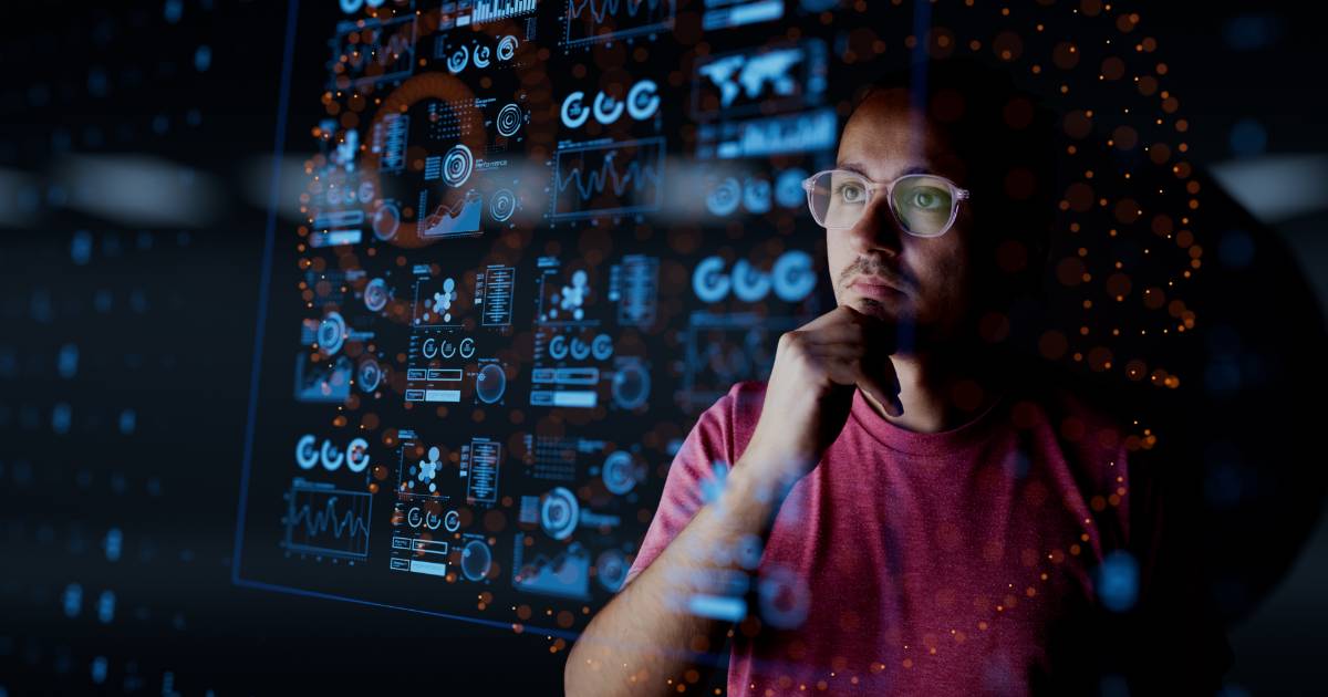 Homem de óculos e camiseta vermelha observa atentamente uma grande tela transparente cheia de gráficos, métricas e dados digitais em tons de azul e laranja, representando análise de dados, métricas de negócios e tecnologia B2B