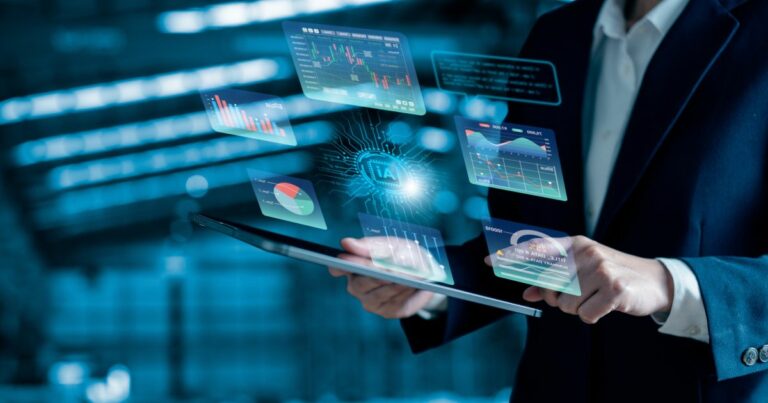Pessoa vestindo terno segura um tablet, do qual são projetadas visualizações holográficas de dados e gráficos. As projeções incluem elementos como gráficos de barras, linhas e ícones digitais. O fundo está desfocado, sugerindo um ambiente interno bem iluminado. (KPMG)