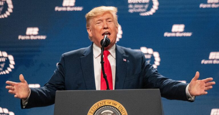 Homem de fato azul escuro, camisa branca e gravata vermelha, a falar ao microfone num púlpito com o selo presidencial dos Estados Unidos, com um fundo azul onde se lê 'Farm Bureau'.