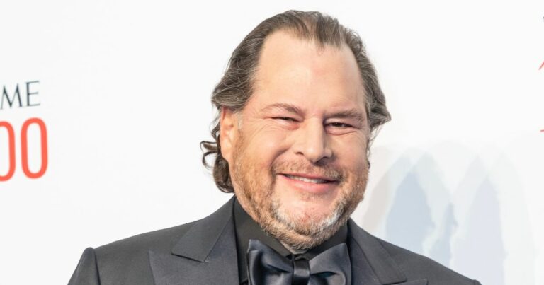 Homem de meia-idade com cabelo castanho ondulado, barba rala e sorriso no rosto, posando para a câmara num evento formal. Ele está vestido com um fato preto elegante e camisa preta, com uma gravata borboleta da mesma cor. O fundo é claro e inclui a palavra “TIME” e o número “100”, indicando que a fotografia foi tirada durante um evento da revista TIME, possivelmente a gala “TIME 100”, que homenageia as 100 pessoas mais influentes do mundo.