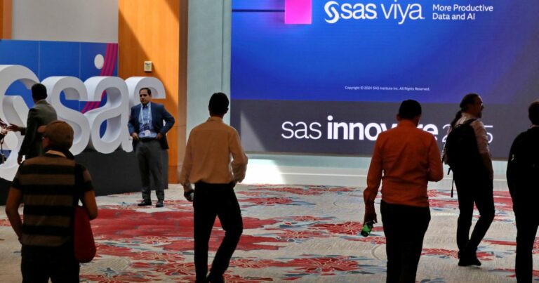 Pessoas circulam pelo saguão do SAS Innovate 2025, evento global de tecnologia e analytics, com destaque para o letreiro da plataforma SAS Viya e a identidade visual do evento projetada em um grande telão digital ao fundo.