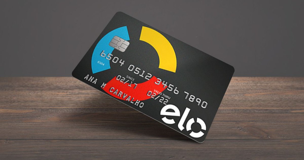 Cartão de crédito da bandeira Elo com fundo preto e elementos gráficos nas cores azul, amarelo e vermelho. O cartão está inclinado sobre uma superfície de madeira. Ele exibe um chip, o número do cartão, datas de validade (02/17 a 02/22) e o nome da titular, Ana M. Carvalho. O logotipo da Elo aparece em branco no canto inferior direito (solução)