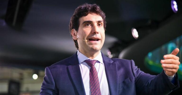Gabriel Galípolo, presidente do Banco Central do Brasil, usa terno azul, camisa branca e gravata listrada em tons de roxo e rosa fala no palco do Febraban Tech 2025 com microfone de lapela preso ao rosto. Ele gesticula com a mão direita e está em um ambiente com iluminação de evento corporativo.