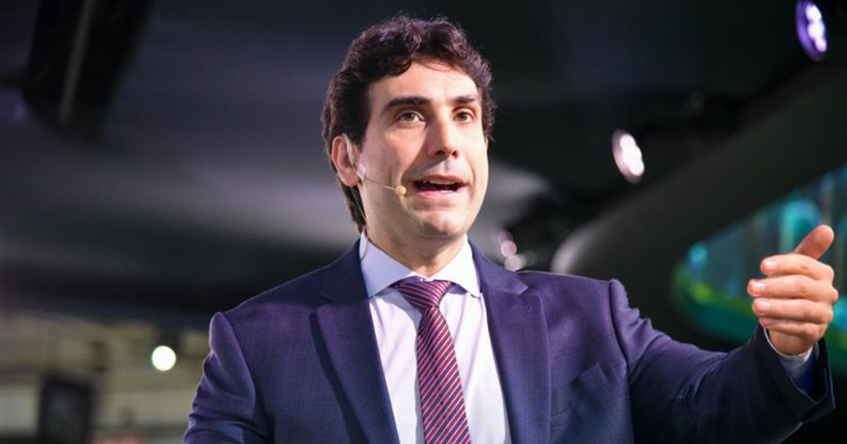 Gabriel Galípolo, presidente do Banco Central do Brasil, usa terno azul, camisa branca e gravata listrada em tons de roxo e rosa fala no palco do Febraban Tech 2025 com microfone de lapela preso ao rosto. Ele gesticula com a mão direita e está em um ambiente com iluminação de evento corporativo.