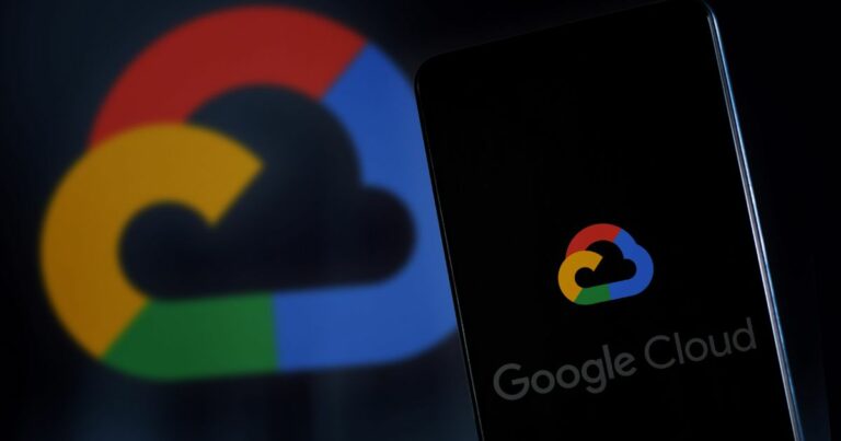 Imagem de um smartphone com a tela exibindo o logotipo do Google Cloud, composto por uma nuvem estilizada com as cores azul, vermelho, amarelo e verde características do Google. Ao fundo, o mesmo logotipo aparece em tamanho ampliado e desfocado, compondo o fundo escuro da imagem. A palavra “Google Cloud” aparece parcialmente na parte inferior da tela do celular. A composição destaca o tema de serviços em nuvem e tecnologia.