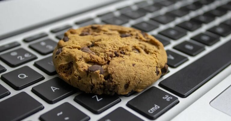 Imagem mostra um cookie de chocolate sobre o teclado de um notebook, especificamente sobre as teclas "A", "Z" e "cmd". A imagem faz uma alusão visual comum ao termo "cookie" utilizado na internet, relacionado a dados armazenados pelo navegador, frequentemente discutidos em contextos de privacidade e vazamento de informações. (cookies)