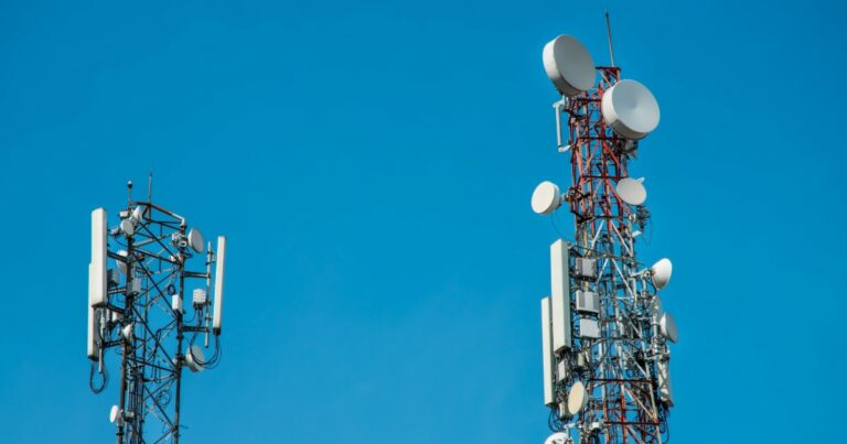 Duas torres de telecomunicação equipadas com diversas antenas e receptores, usadas para transmissão de sinais de rede, como 4G. As estruturas metálicas estão posicionadas contra um céu azul claro, representando infraestrutura de comunicação e conectividade móvel (rodovias)