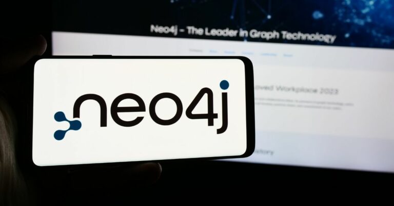 A imagem mostra um smartphone exibindo o logotipo da Neo4j, sistema de gerenciamento de banco de dados orientado a grafos. O logotipo inclui o texto "neo4j" com um ponto azul estilizado e nós conectados formando parte da letra "n". Ao fundo, há uma tela desfocada que parece ser um site ou slide de apresentação, com o título "Neo4j – The Leader in Graph Technology". A composição destaca a marca e o posicionamento da Neo4j como líder em tecnologia de grafos.