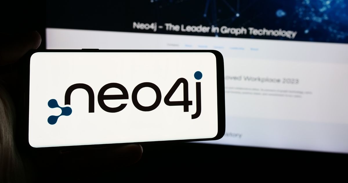 A imagem mostra um smartphone exibindo o logotipo da Neo4j, sistema de gerenciamento de banco de dados orientado a grafos. O logotipo inclui o texto "neo4j" com um ponto azul estilizado e nós conectados formando parte da letra "n". Ao fundo, há uma tela desfocada que parece ser um site ou slide de apresentação, com o título "Neo4j – The Leader in Graph Technology". A composição destaca a marca e o posicionamento da Neo4j como líder em tecnologia de grafos.