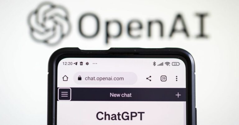 A imagem mostra um smartphone exibindo a página chat.openai.com, com a interface do ChatGPT aberta e o título “New chat” visível na parte superior. O dispositivo está em primeiro plano, com detalhes como ícones de bateria, sinal e hora na barra superior. Ao fundo, desfocado, aparece o logotipo da OpenAI, composto pelo nome “OpenAI” em letras pretas e o símbolo característico da marca. A composição sugere um contexto relacionado a inteligência artificial e tecnologia, destacando a integração entre dispositivos móveis e plataformas de IA.