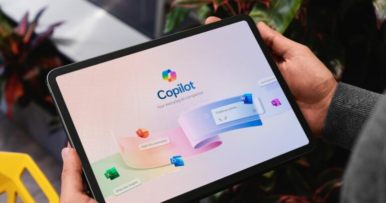 A imagem mostra um tablet sendo segurado com ambas as mãos, exibindo a interface do Microsoft Copilot com o texto “Copilot – Your everyday AI companion”. A tela apresenta um design limpo e moderno, com fundo claro e elementos gráficos coloridos que representam aplicativos do pacote Microsoft 365, como Word, Excel, PowerPoint e Outlook, sugerindo integração e produtividade. O cenário ao redor inclui detalhes de um ambiente interno com plantas e uma cadeira amarela parcialmente visível, transmitindo um clima contemporâneo e descontraído. A iluminação é natural, destacando bem o dispositivo e a interface.