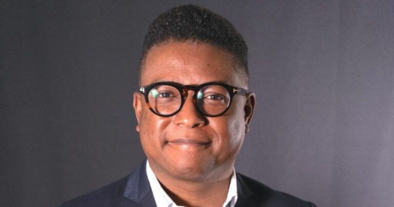 A imagem mostra uma pessoa vestindo traje formal, com uma camisa clara e um blazer escuro, em frente a um fundo neutro, sugerindo um cenário corporativo ou profissional. (Coca-Cola)