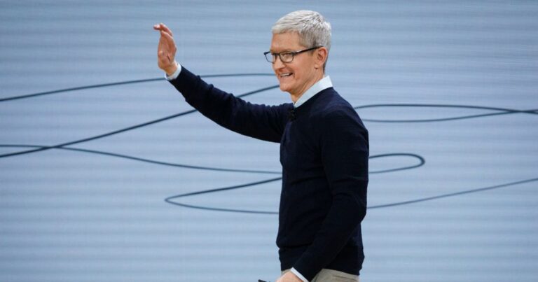 A cena mostra uma pessoa em um palco ou ambiente de apresentação, aparentemente durante um evento ou conferência tecnológica. O fundo é claro, com linhas curvas pretas que parecem fazer parte de um design minimalista. (Apple)